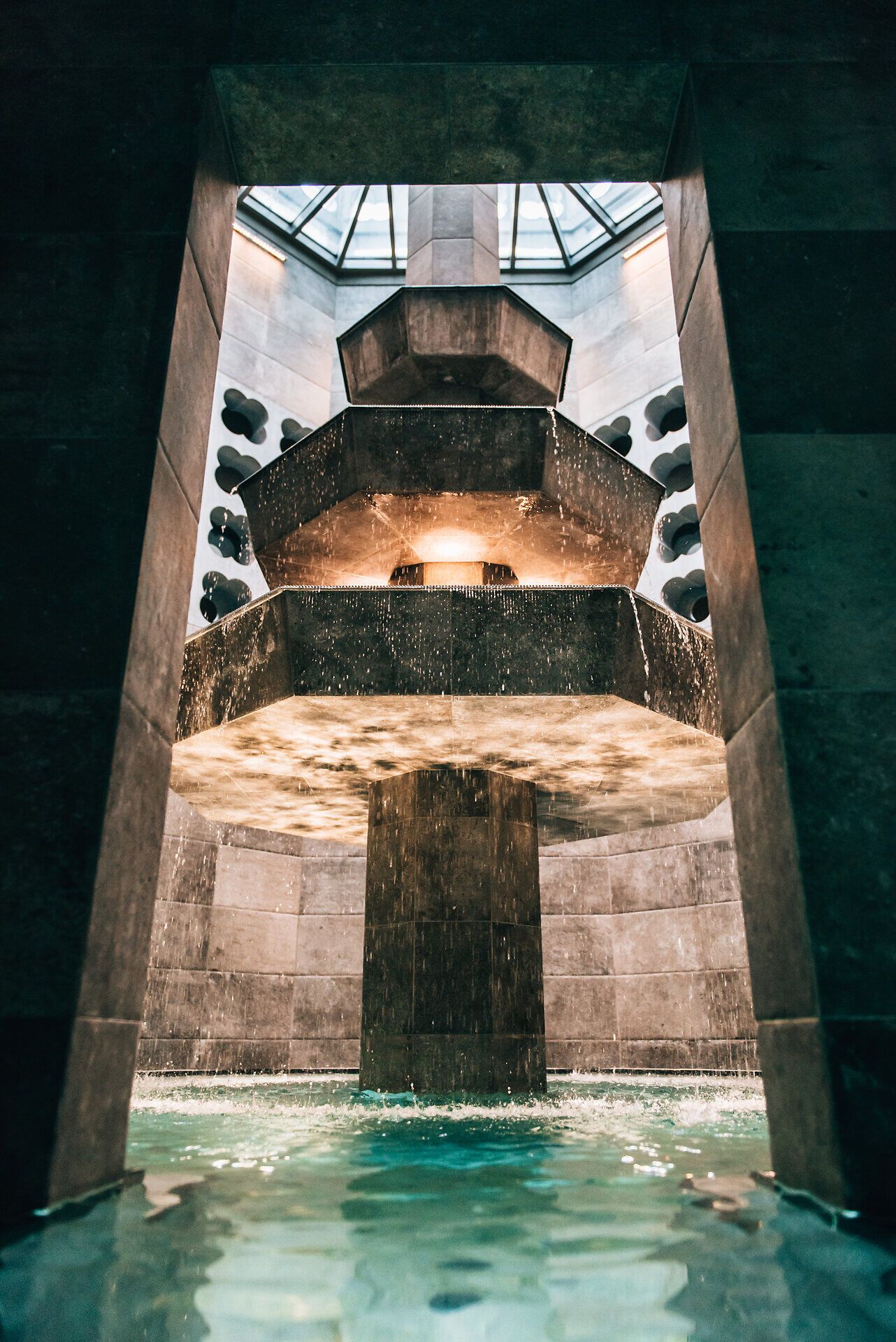 Ein beeindruckender Wasserfall fließt sanft in das ruhige Becken, umgeben von stilvollem Stein und sanftem Licht. Die Atmosphäre ist entspannend und lädt dazu ein, die Seele baumeln zu lassen und die Hektik des Alltags hinter sich zu lassen.