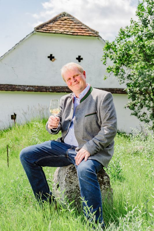 Man sitting on a stone in the green, holding a wine glass in his hand.