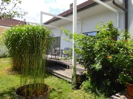 Terrasse mit Pflanzen und Gartenmöbeln vor einem weißen Haus.