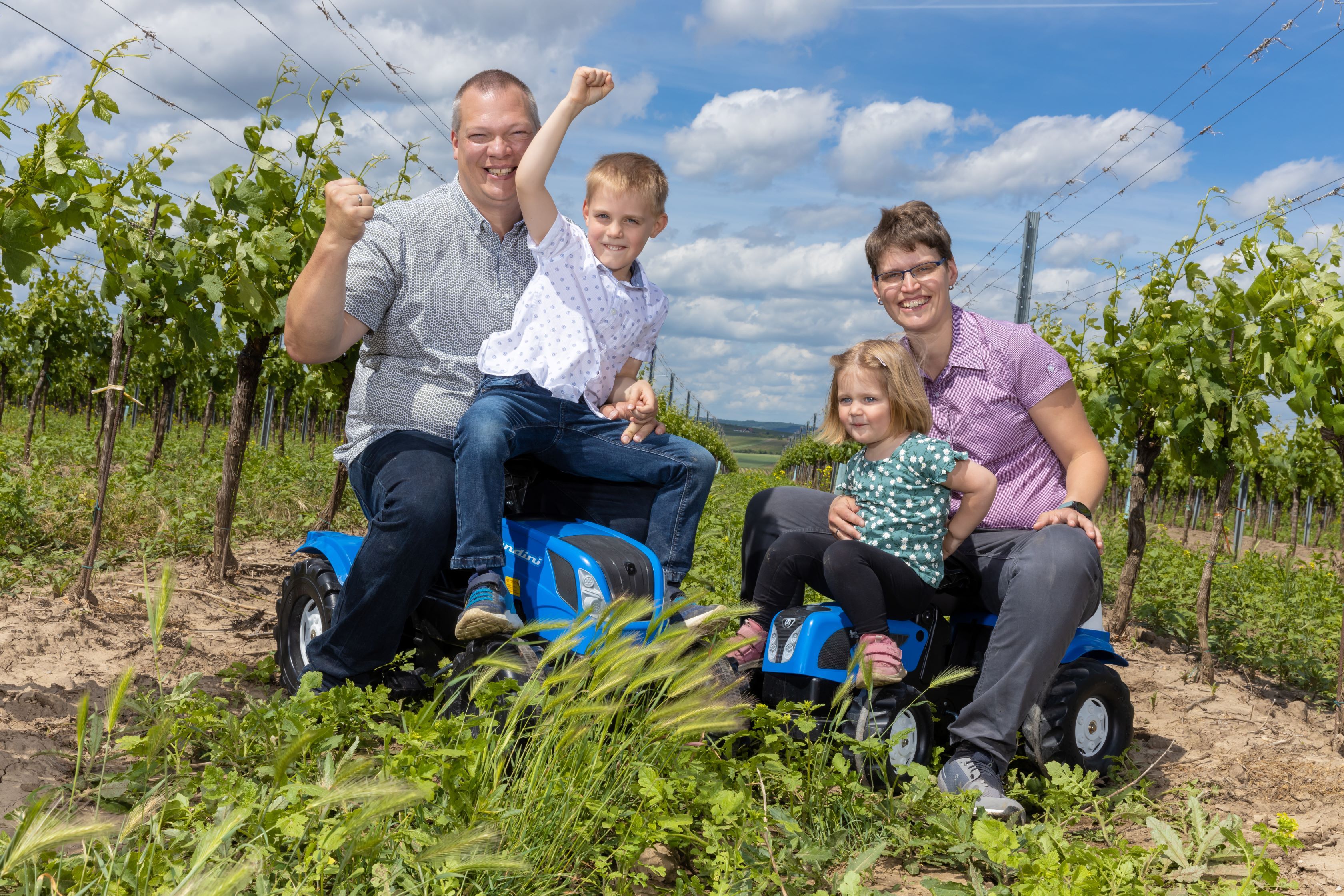 Family sitting on toy tractors in the vineyard.