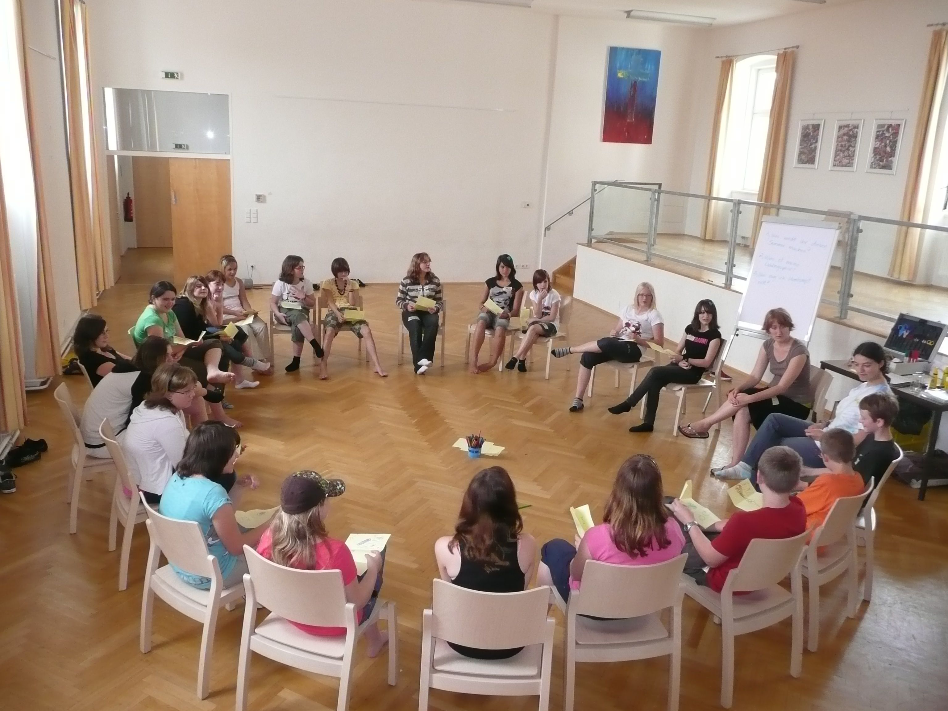 Ľudia sedia v kruhu stoličiek vo veľkej miestnosti.