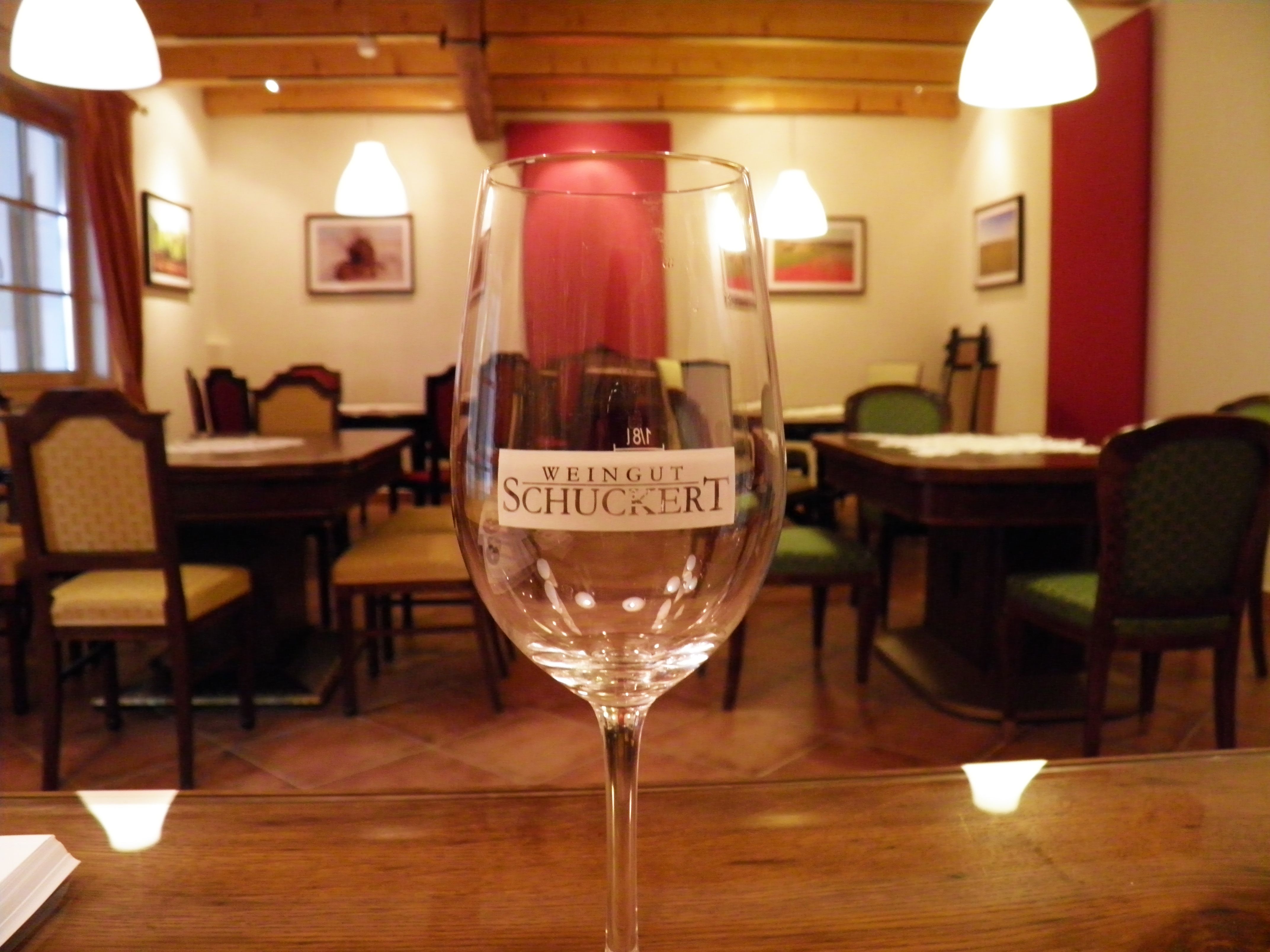 Weinglas mit Aufschrift "Weingut Schuckert" in einem gemütlichen Raum mit Holzmöbeln und Bildern an der Wand.