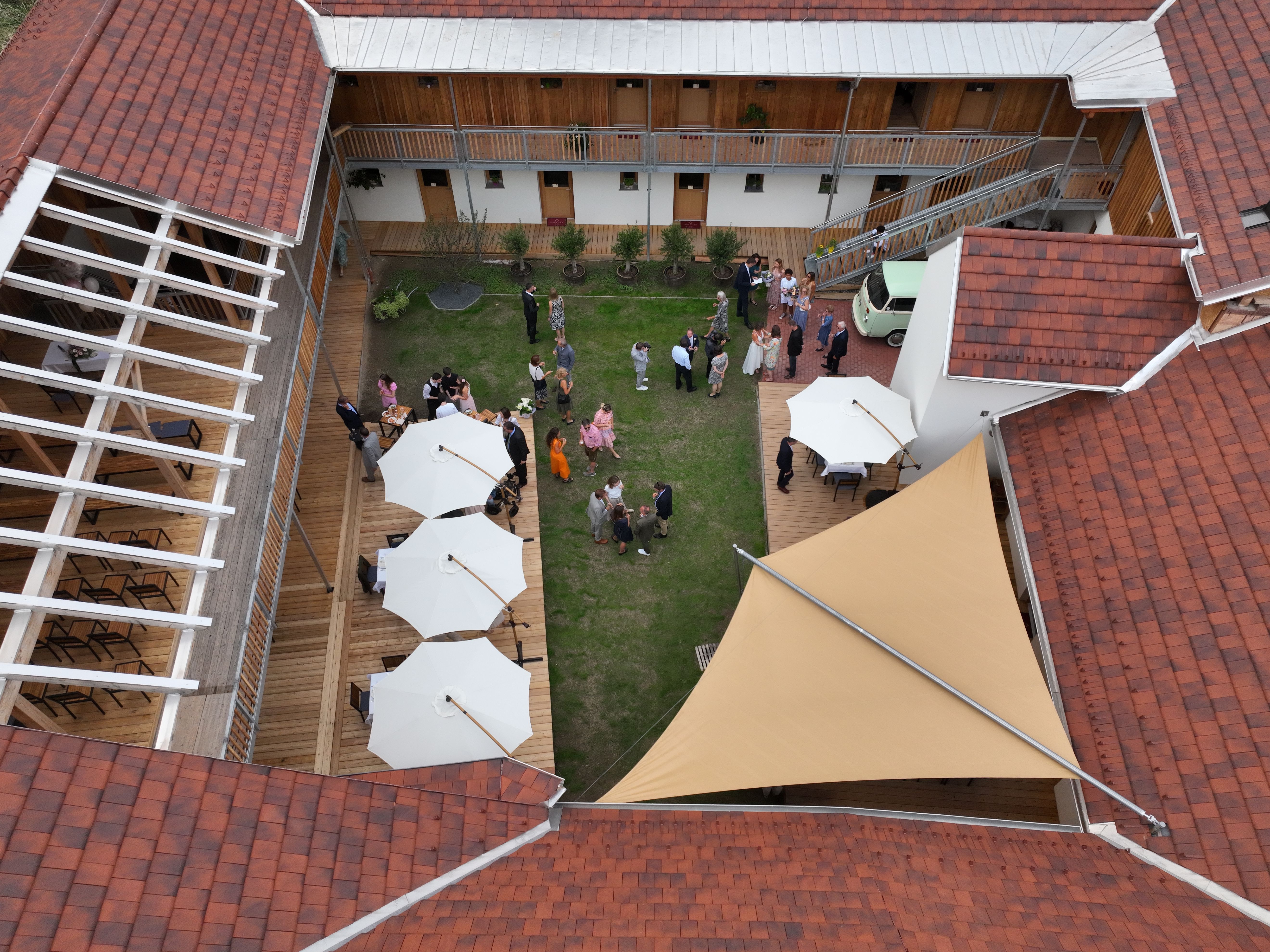 Bird's eye view of the inner courtyard with green lawn, white parasols and guests at a reception.