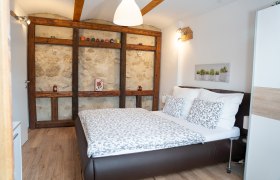 Gemütliches Schlafzimmer mit Holzbalken, Steinwand und modernem Bett.