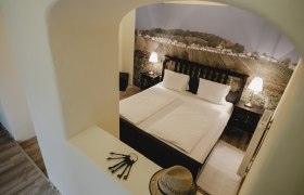 Ein gemütliches Schlafzimmer mit Doppelbett, zwei Nachttischlampen und einer Wandtapete mit Weinlandschaft.