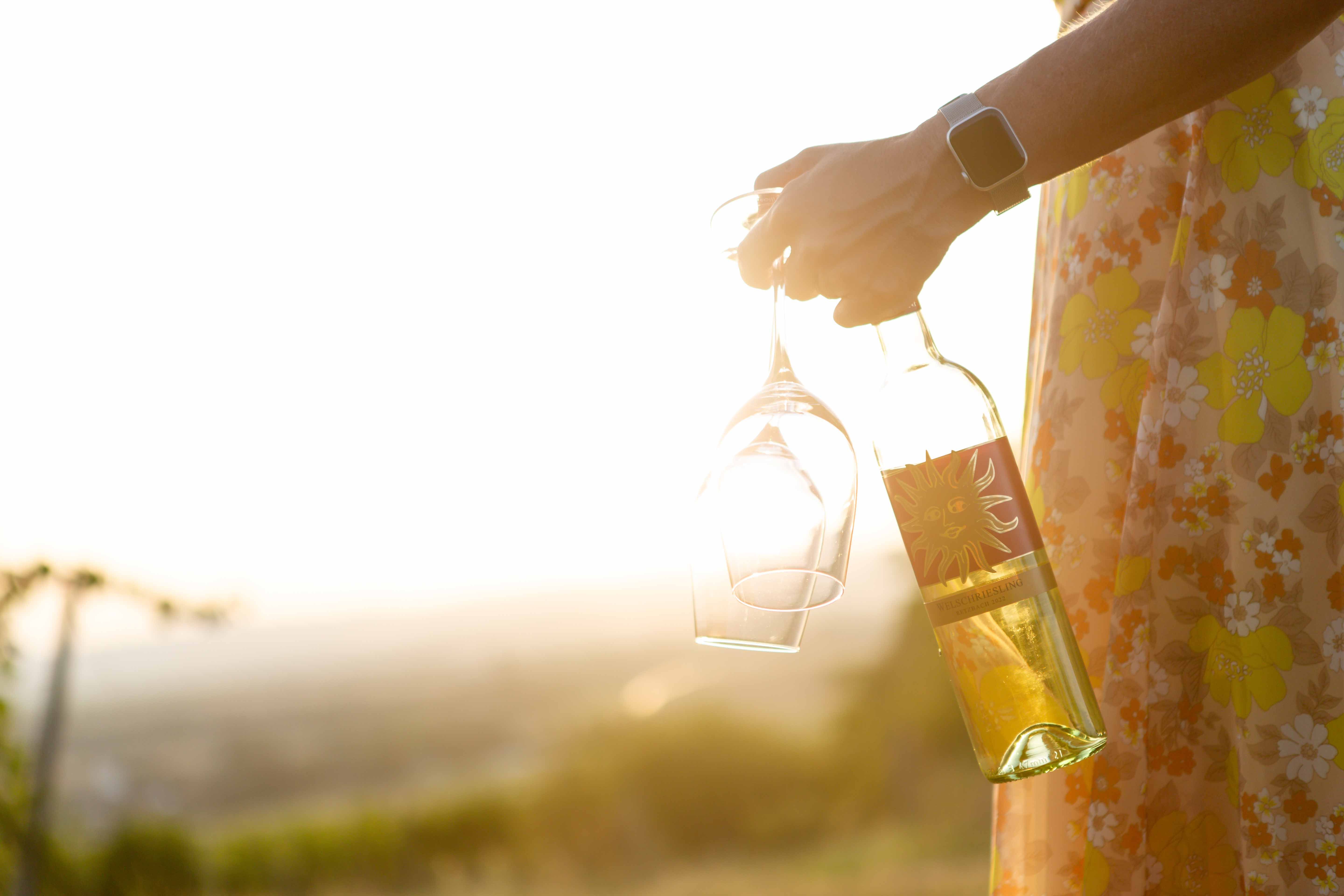 Person holding wine bottle and glasses in the sunset.