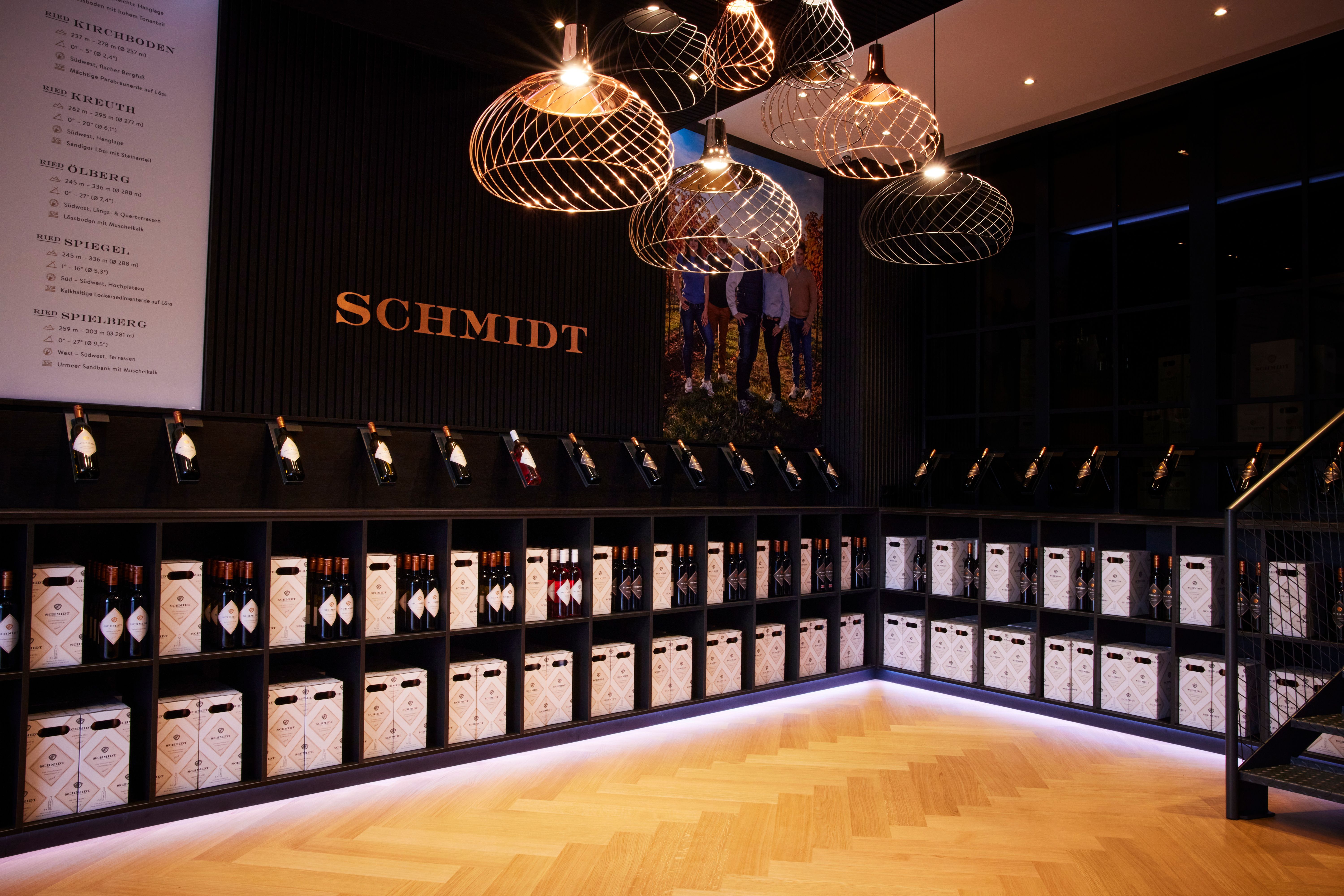 Weinregal mit Flaschen und Kartons in einem stilvollen Raum mit dem Schriftzug 'Schmidt'.