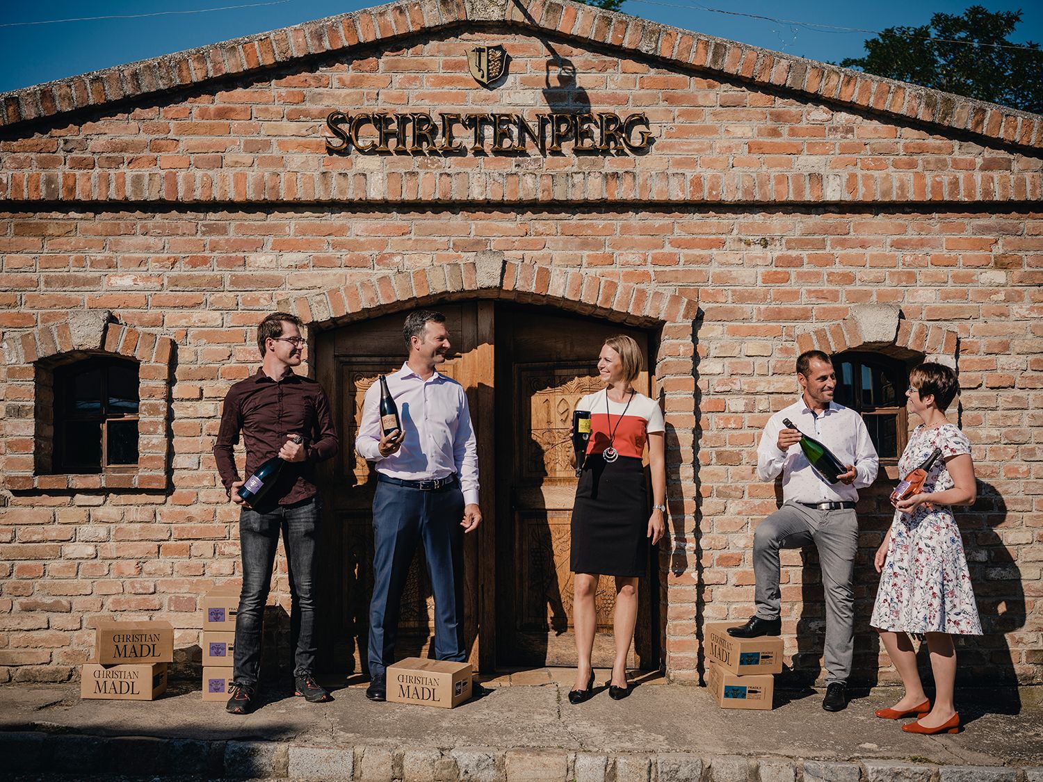 Fünf Personen stehen vor einem Backsteingebäude mit Sektflaschen in der Hand.