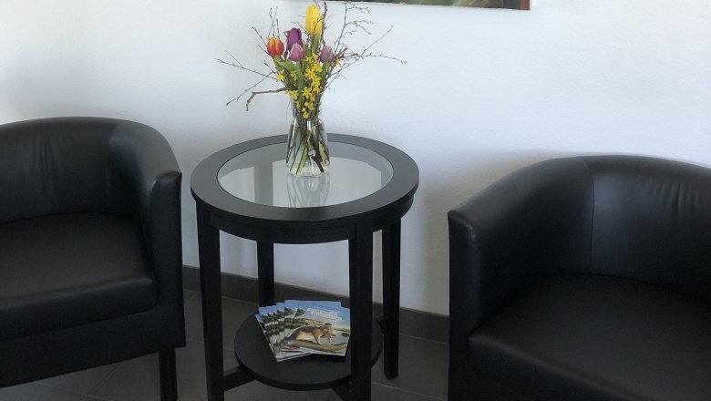 Zwei schwarze Sessel und ein runder Tisch mit Blumen in einem Raum. An der Wand hängt ein abstraktes Gemälde mit Fuchs-Motiv.