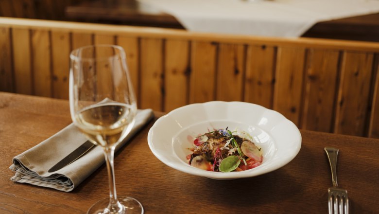 Ein Glas Weißwein neben einem Teller mit einem dekorativen Gericht auf einem Holztisch.