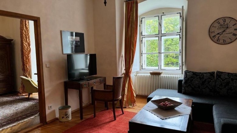 Gemütliches Gästezimmer mit Sofa, Tisch, Fernseher und großem Fenster.