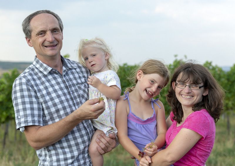 A family stands smiling in a vineyard.