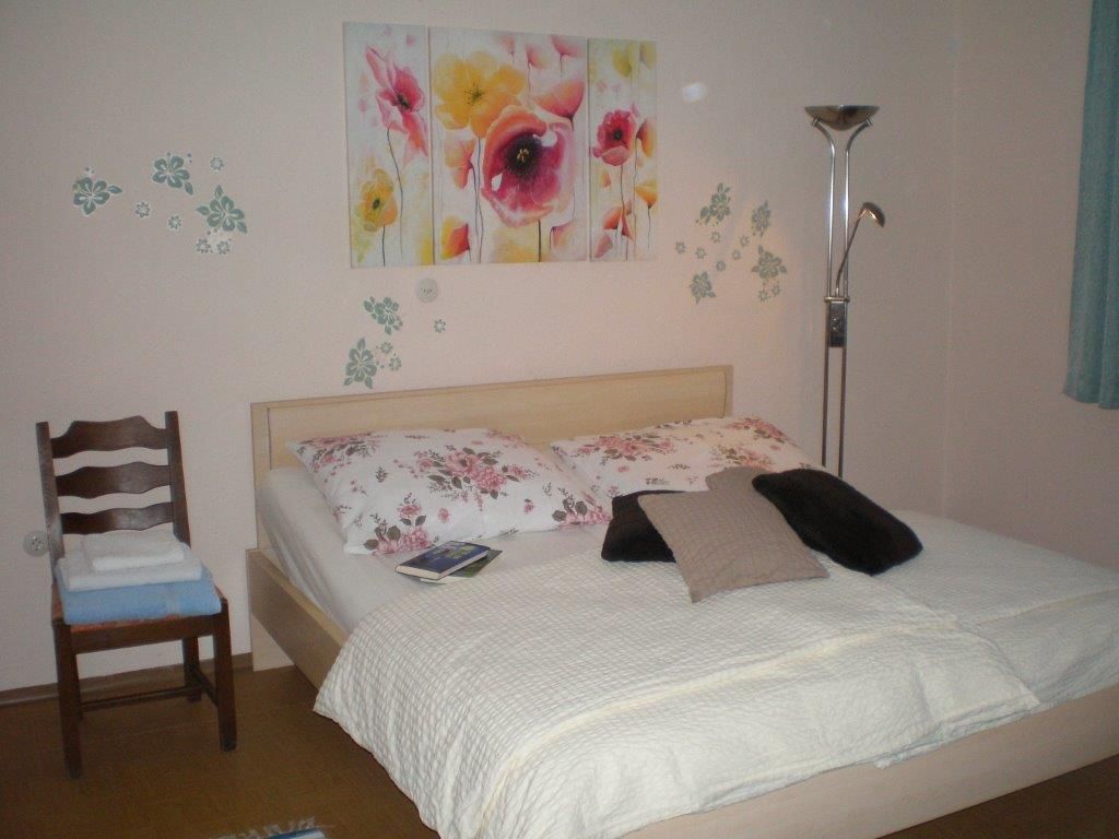 Ein gemütliches Gästezimmer mit einem Doppelbett, dekoriert mit floralen Kissen und einem Blumenbild an der Wand.