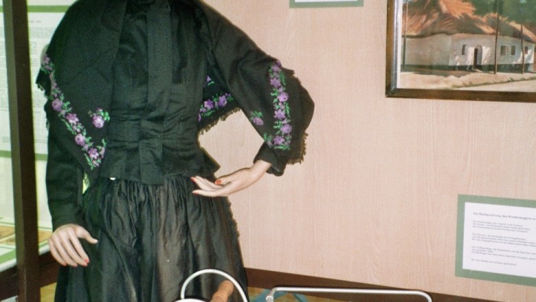 Eine Schaufensterpuppe in traditioneller Kleidung neben einem alten Kinderwagen in einem Ausstellungsraum.