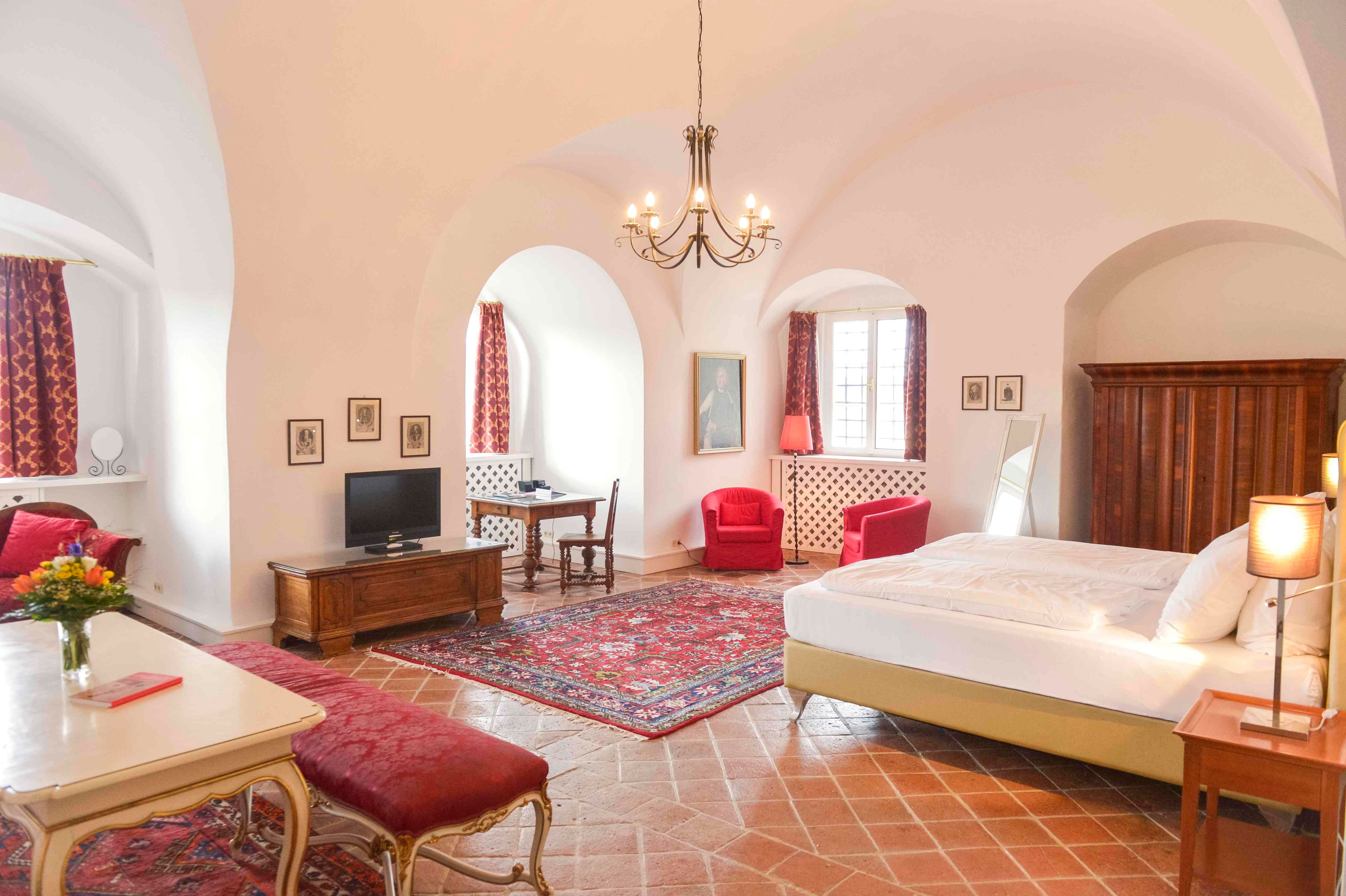 Luxuriöse Suite mit antiken Möbeln, roten Teppichen und Vorhängen, einem großen Bett und einem Kronleuchter.