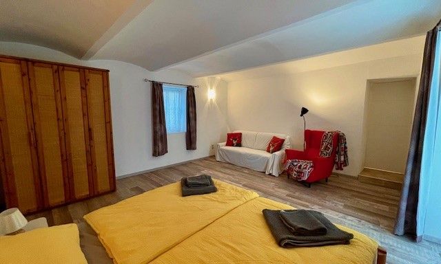 Ein Schlafzimmer mit Doppelbett, gelber Bettwäsche, Holzschrank, rotem Sessel und weißem Sofa.