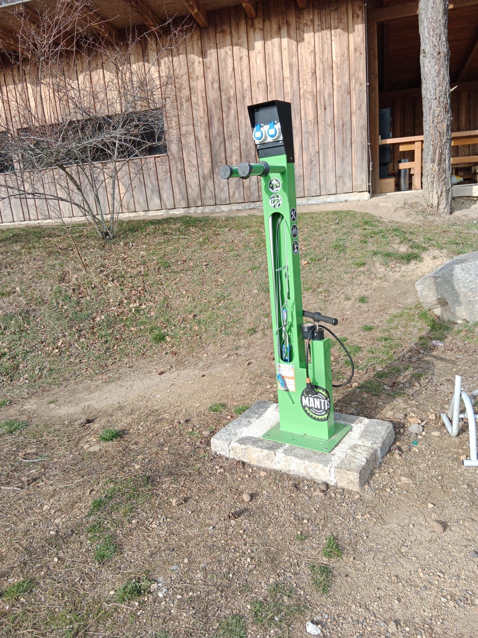 Grüne E-Bike-Ladestation vor einem Holzgebäude.