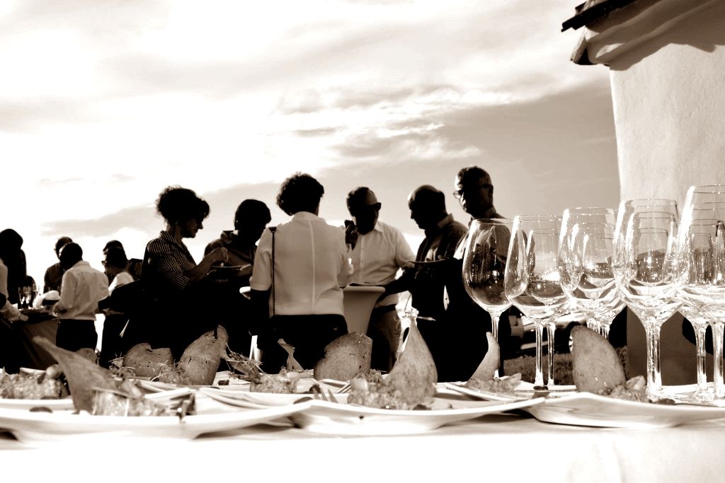 Menschen bei einer Veranstaltung im Freien mit Weingläsern und Snacks auf einem Tisch.