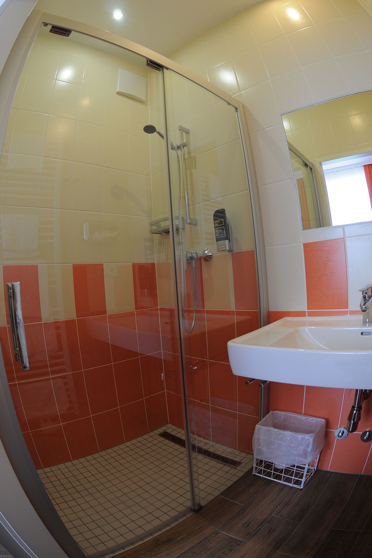 Badezimmer mit Dusche, Waschbecken und orange-weißen Fliesen.