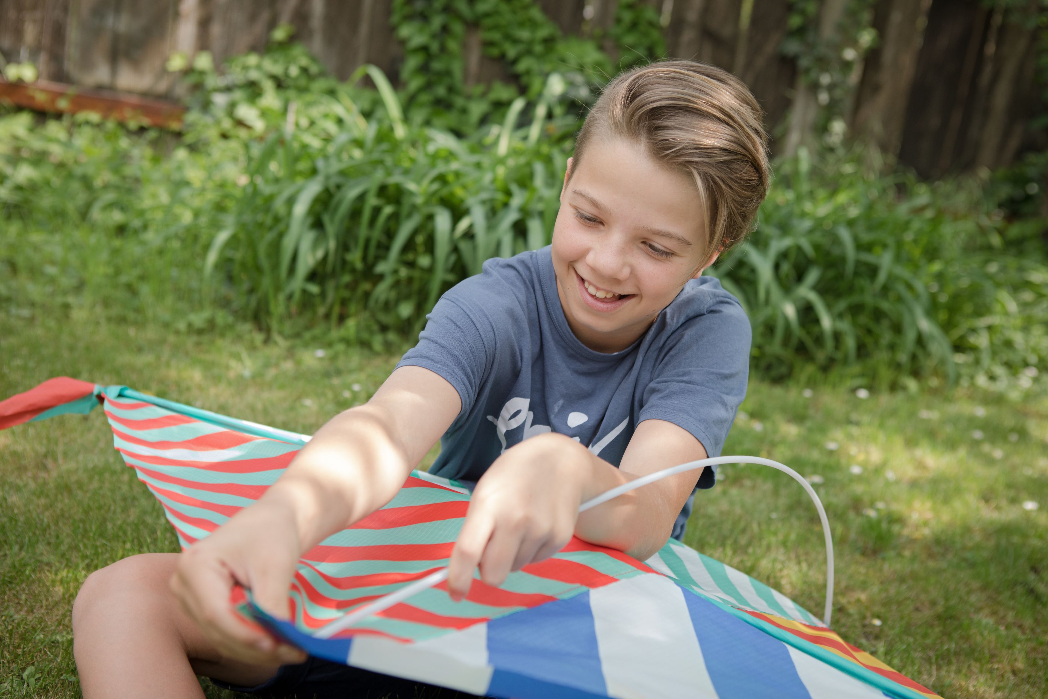 A child sits in the grass and holds a colorful kite in his hands.
