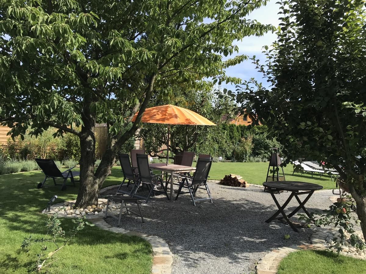 Garten mit Sitzbereich unter Bäumen, Tisch und Stühlen, orangefarbener Sonnenschirm.