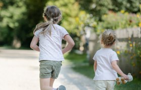 Zwei Kinder laufen auf einem Kiesweg in einem grünen Park.