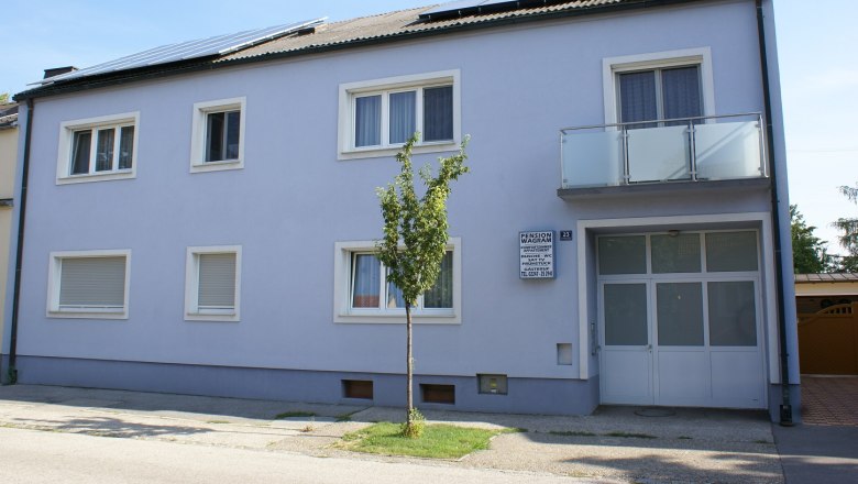 Außenansicht eines zweistöckigen Gebäudes mit blauer Fassade und Solarpanels auf dem Dach.