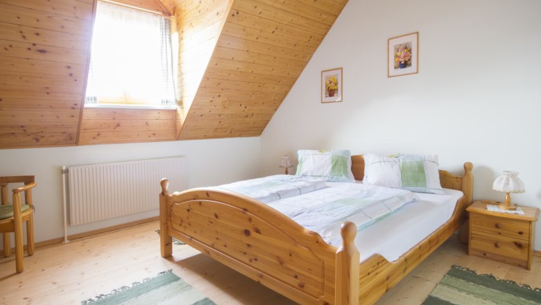 Double room, © Winzerhof Semmler Cozy bedroom with wooden furniture and sloping ceiling.