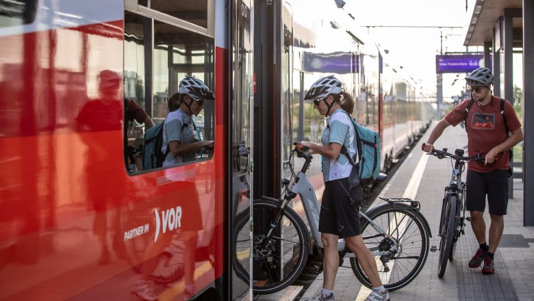 Two cyclists get on a train with their bicycles.