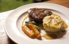 Ein Teller mit einem Stück Fleisch, Gemüse und einem Kartoffelgratin.