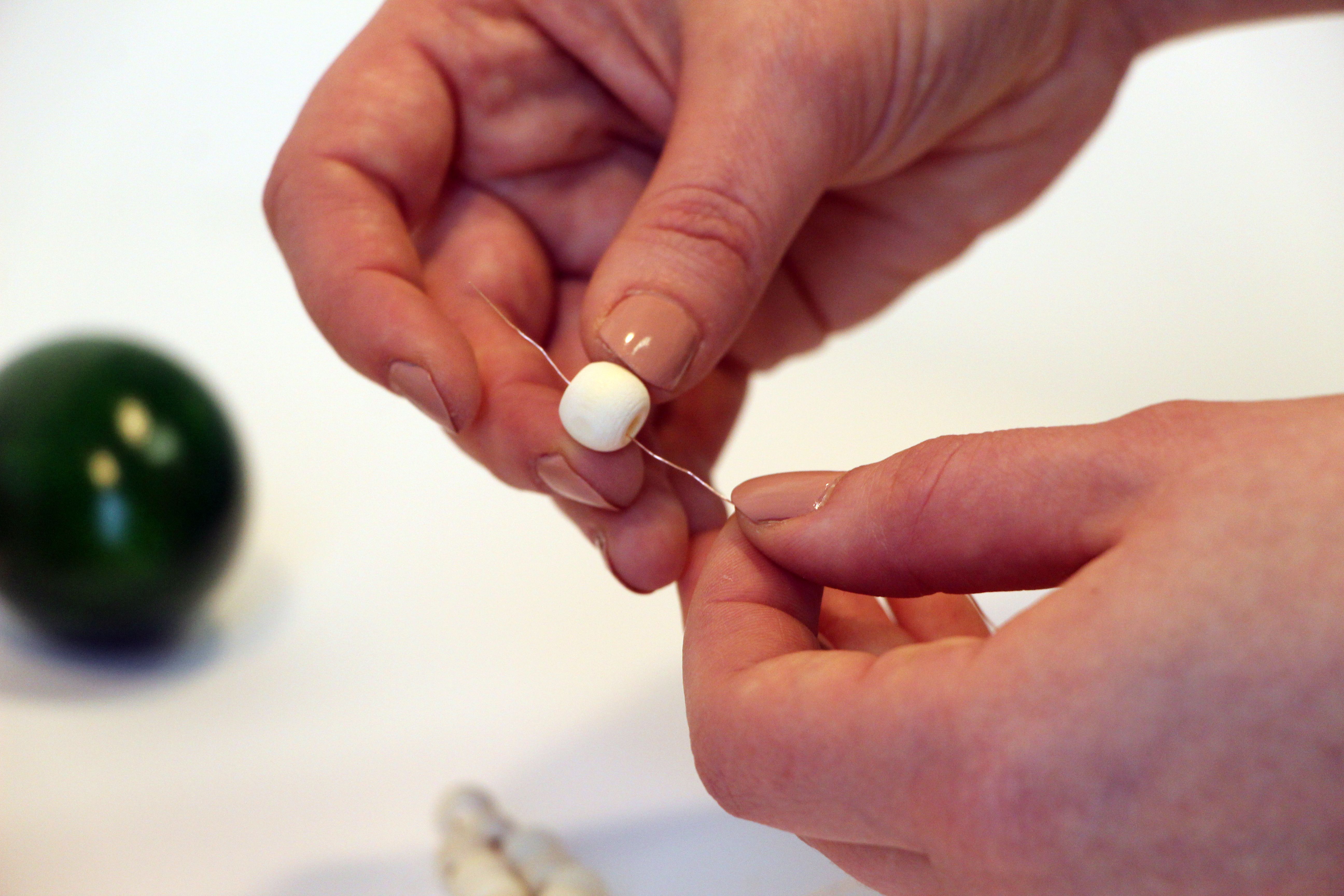 Auf Draht wird eine Holzperle aufgefädelt.