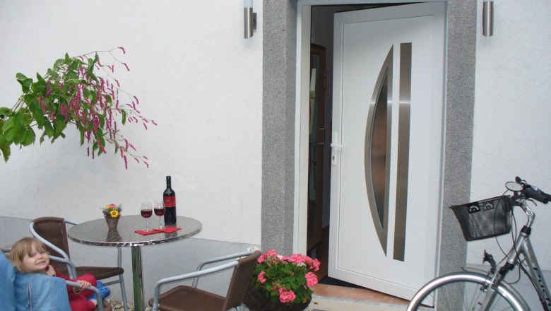 Ein offener Hauseingang mit Tisch, Stühlen, Weinflasche und Fahrrad.