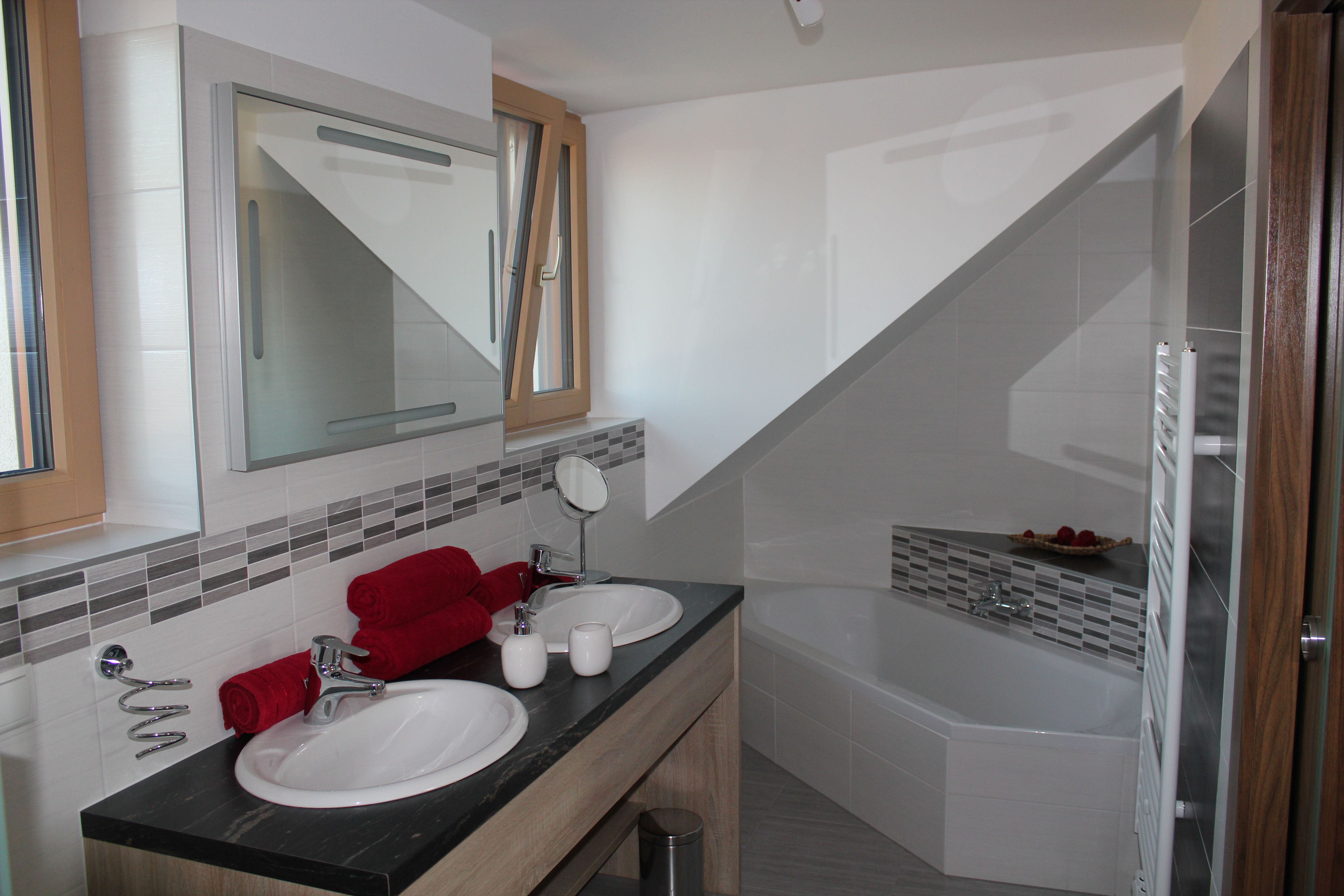 Modernes Badezimmer mit Doppelwaschbecken, Badewanne und roten Handtüchern.