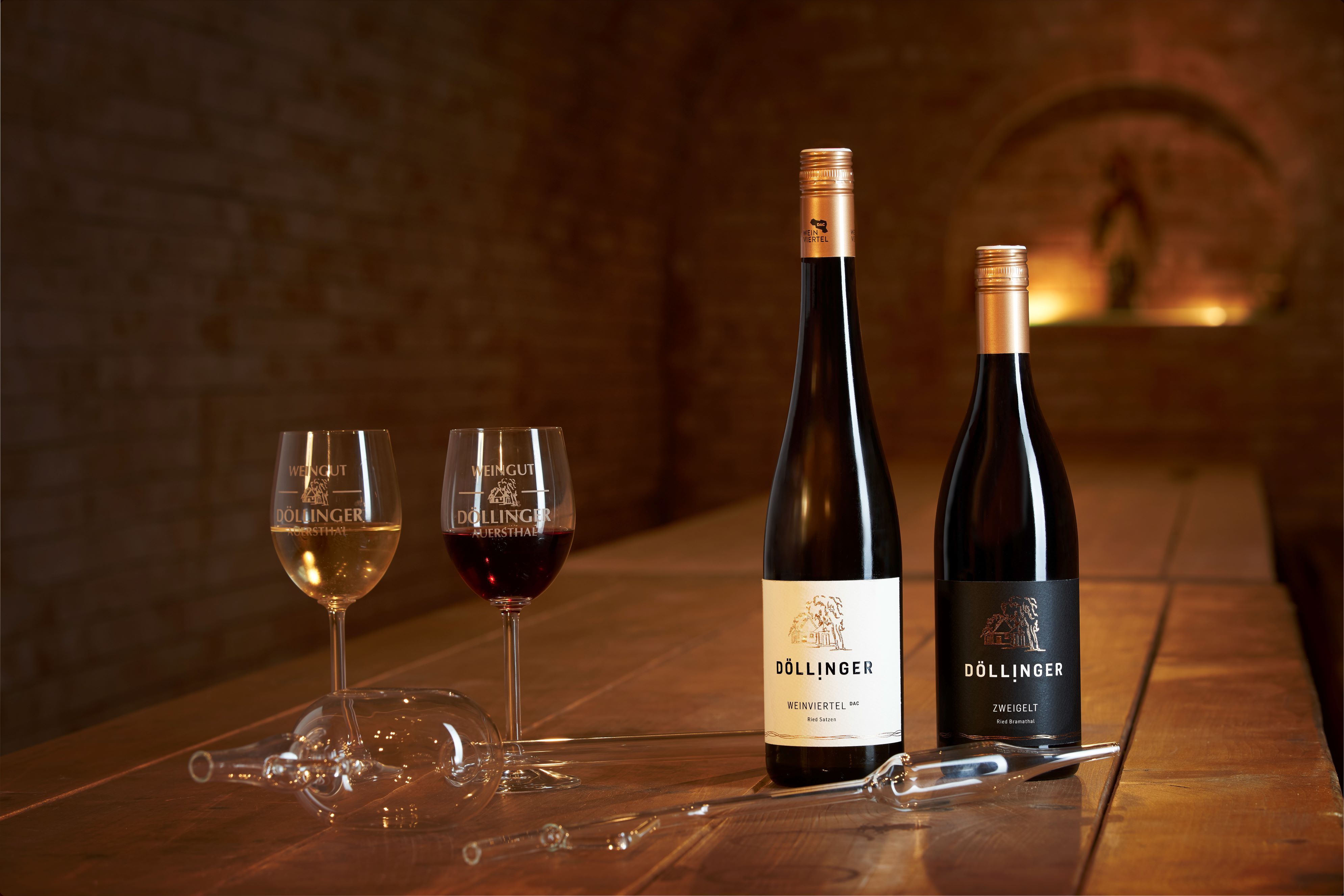 Two wine glasses and two wine bottles on a wooden table in a wine cellar.