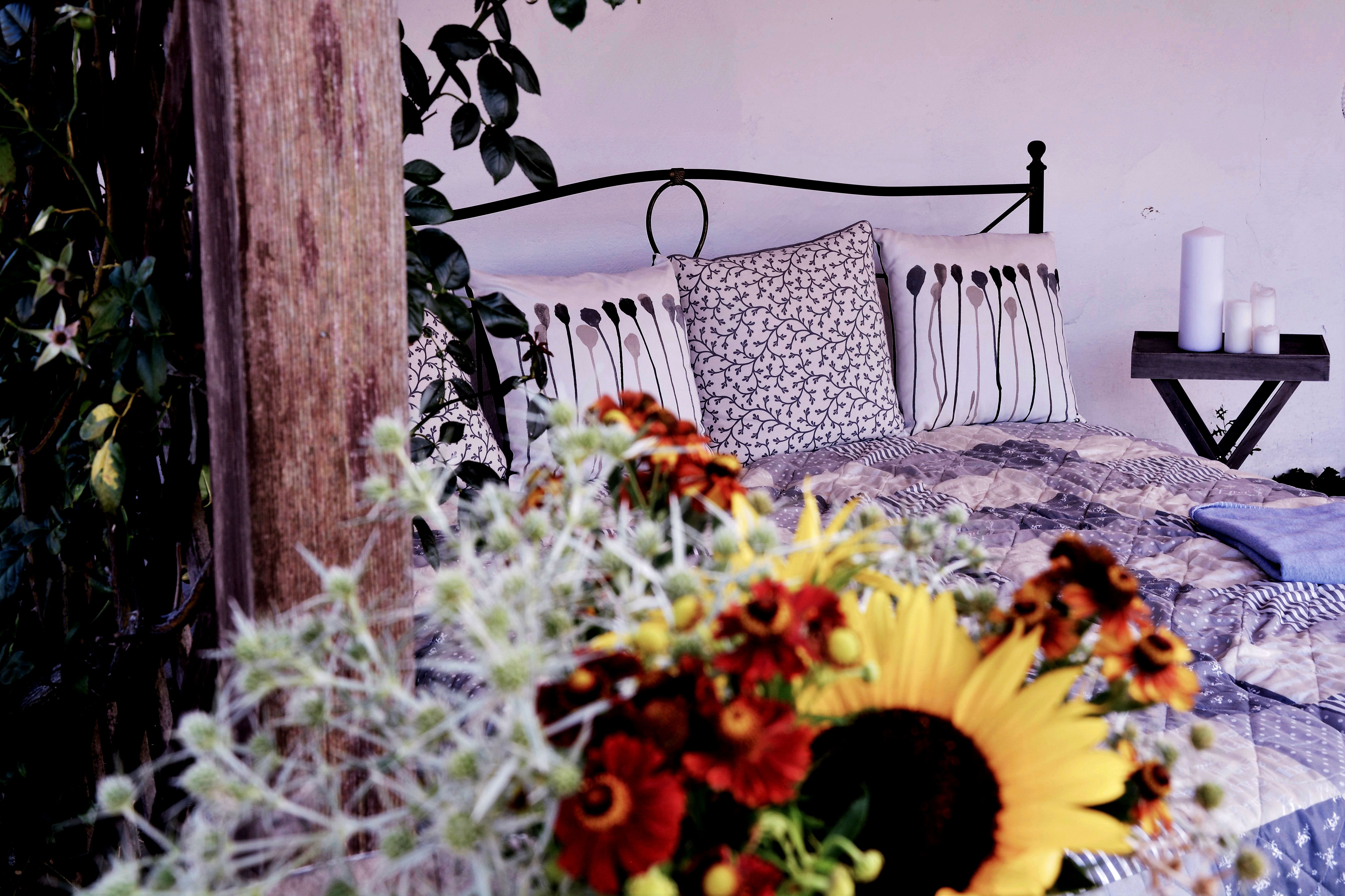 Gemütliches Bett mit dekorativen Kissen und Blumen im Vordergrund.