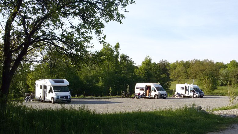 Motorhomes on a pitch in the countryside, surrounded by trees.