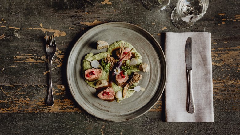 A plate of saddle of venison, coriander cream and vegetables on a rustic table.