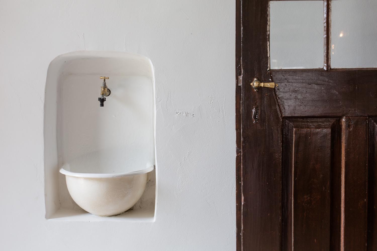 Ein alter Wasserhahn über einem eingelassenen Becken neben einer Holztür.