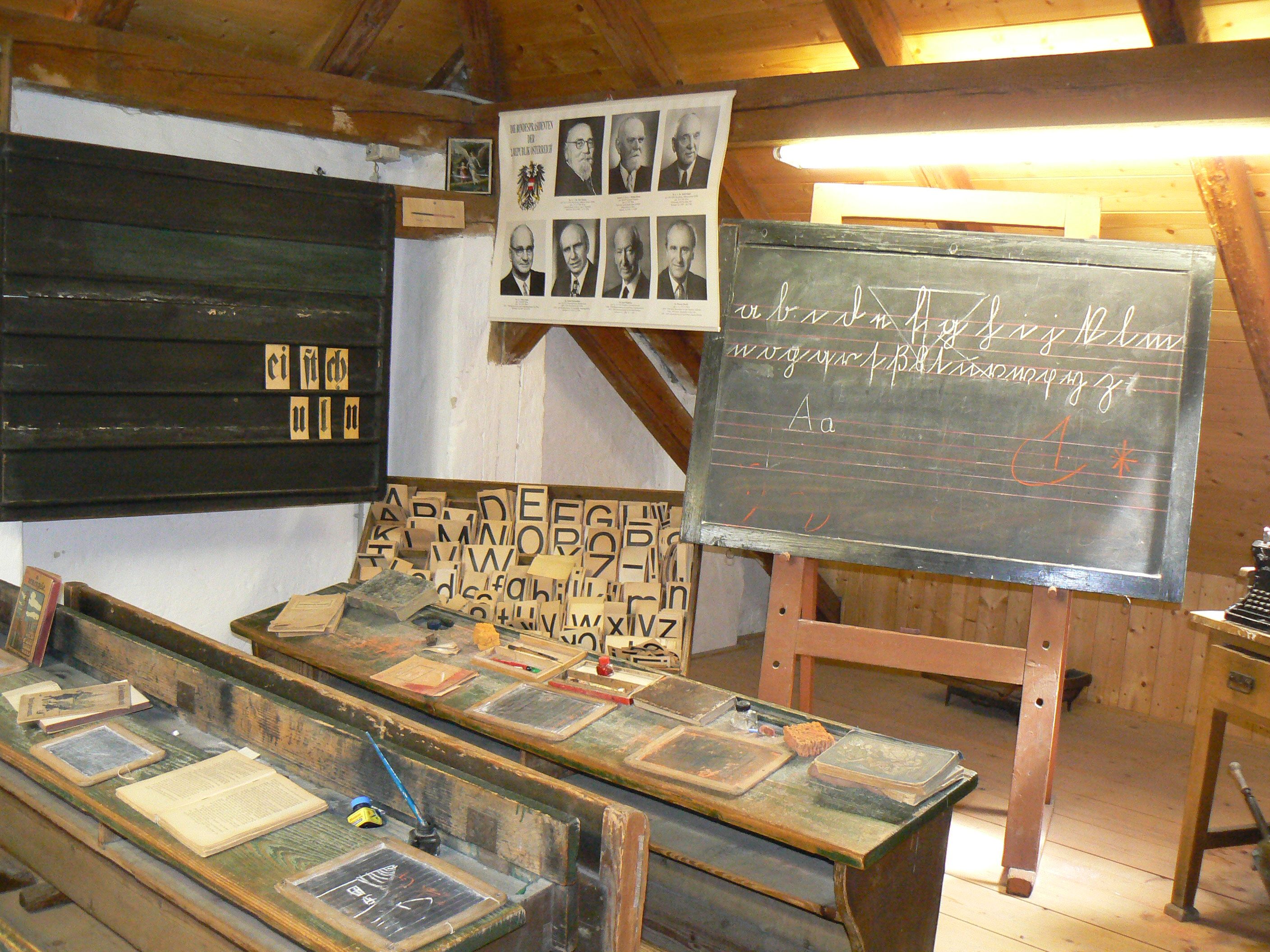 Historisches Klassenzimmer mit Schultafel, Pult und Lehrmaterialien.