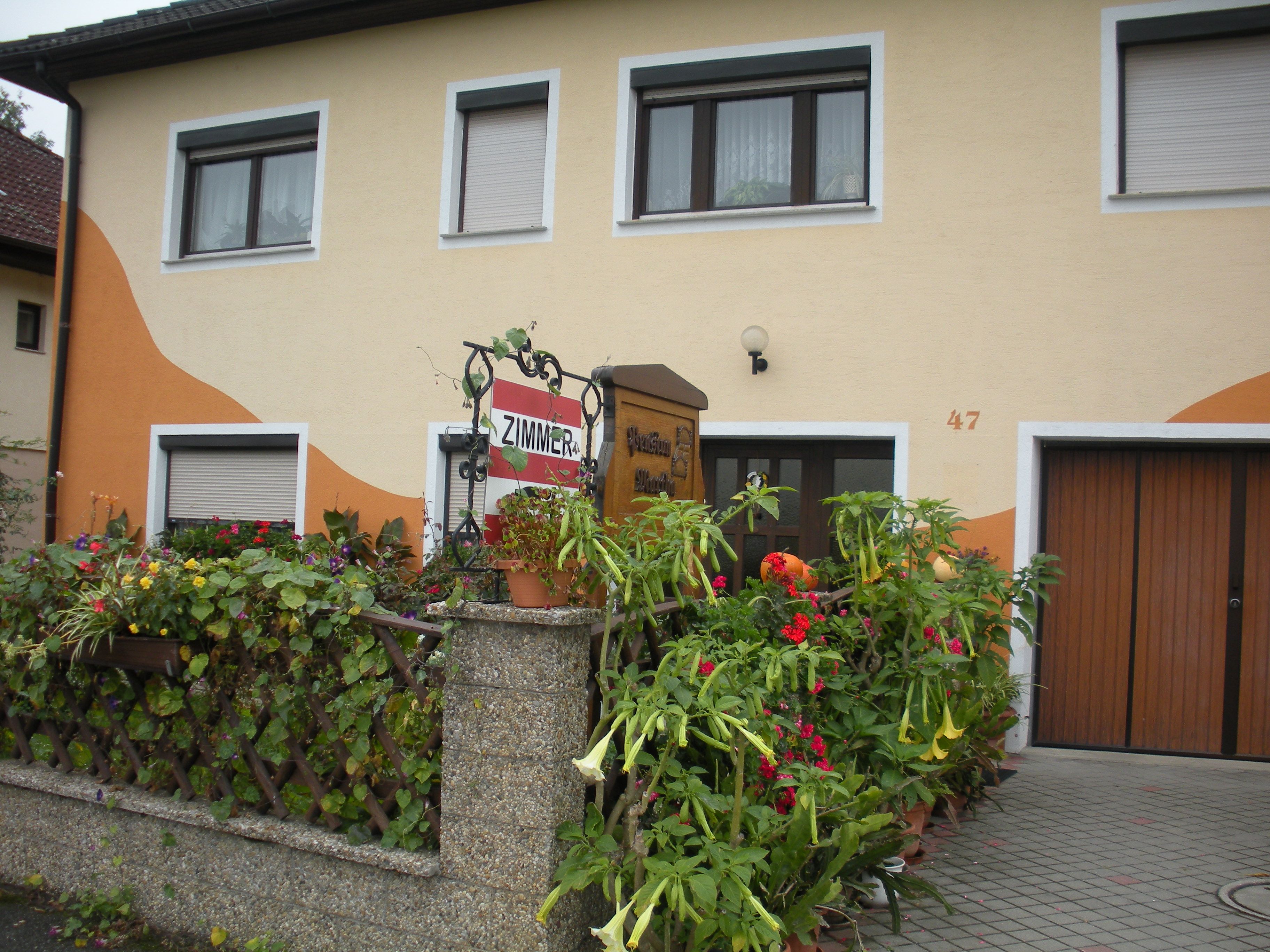 Haus mit gelber Fassade, Blumendekoration und Schild 'Zimmer'.