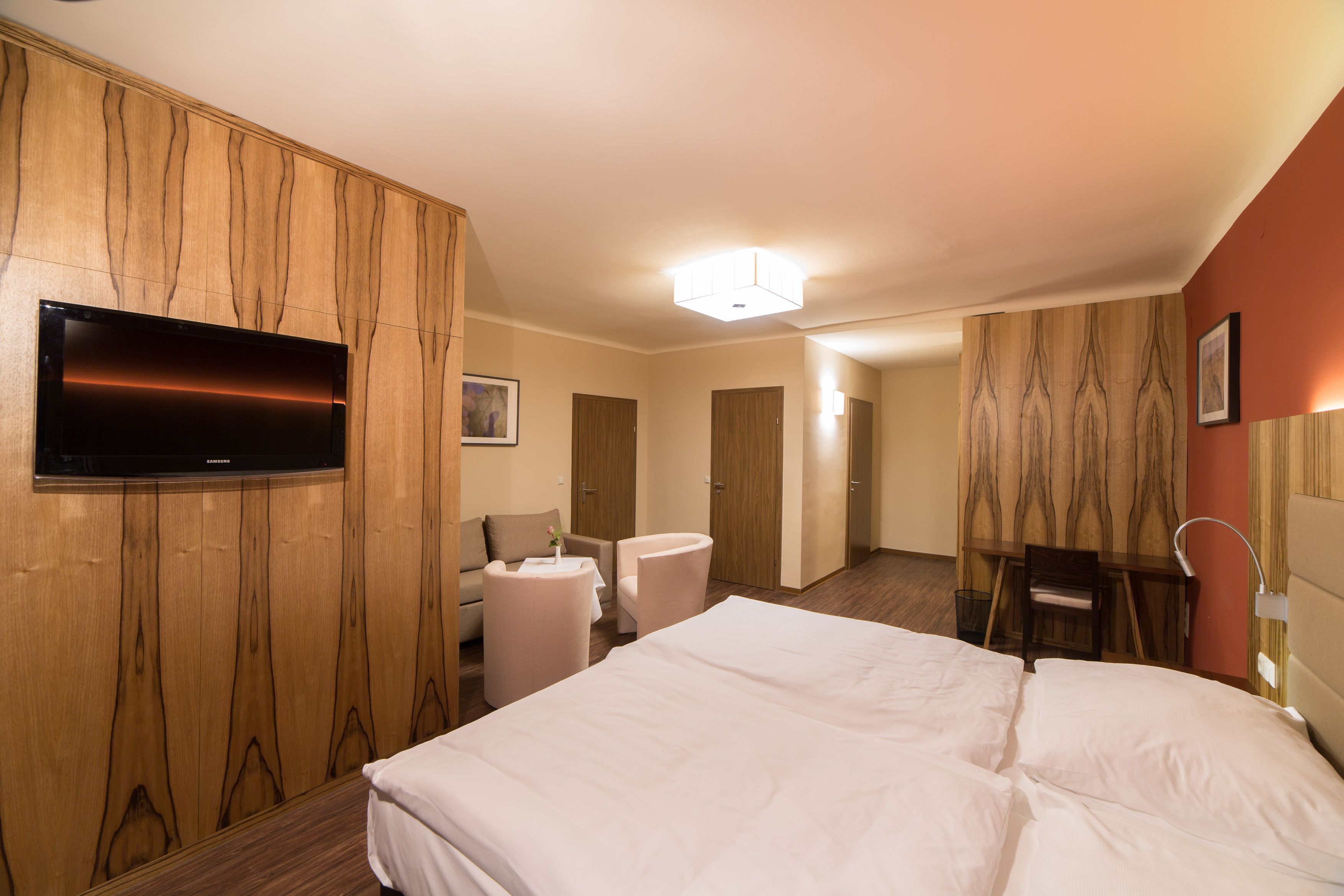 Modern eingerichtetes Hotelzimmer mit Doppelbett, Fernseher, Sitzbereich und Holzmöbeln.