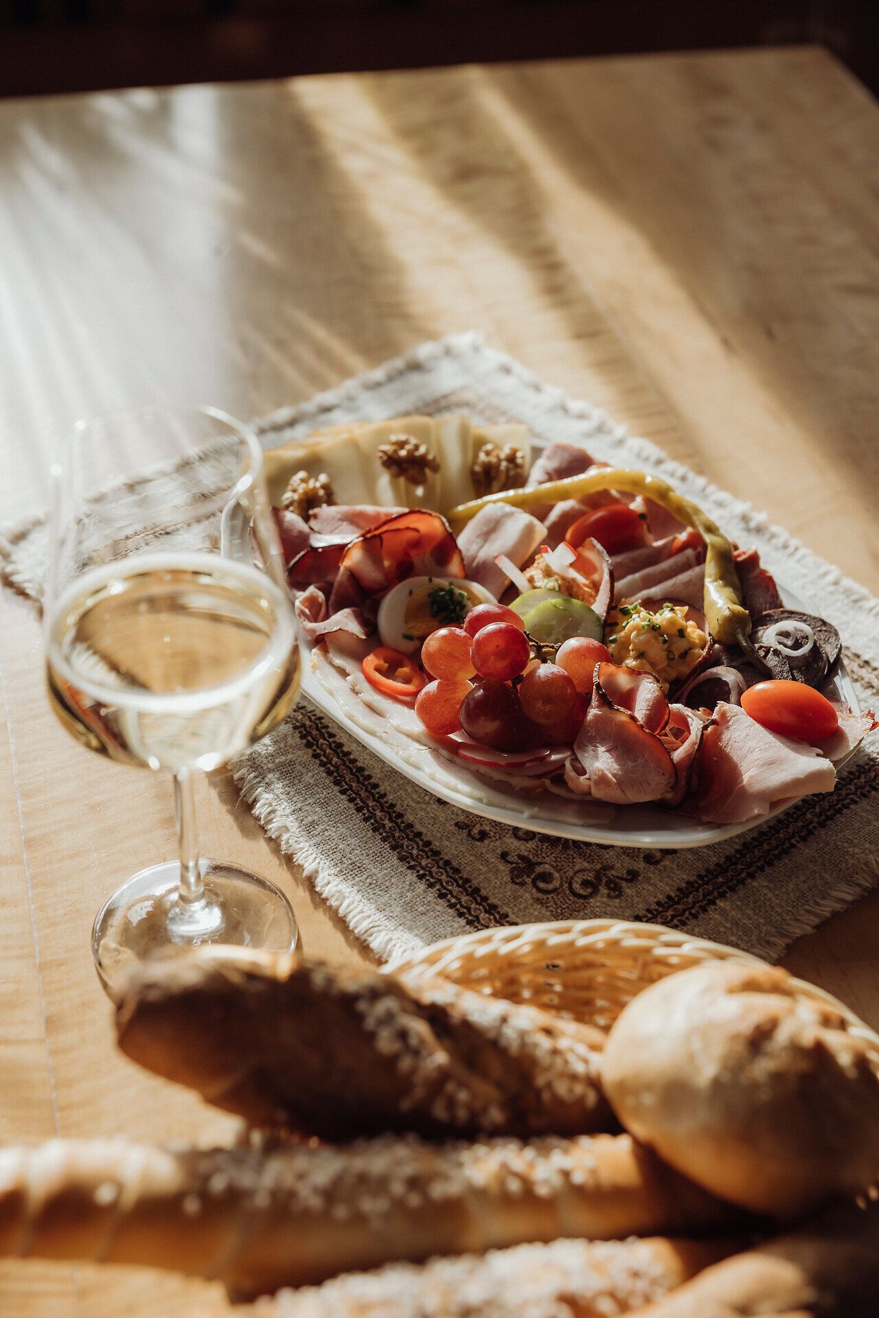 Genießen Sie die köstliche Brettljause, die mit frischen regionalen Zutaten zubereitet wurde, während Sie in entspannter Atmosphäre ein Glas Wein nippen. Die warmen Sonnenstrahlen tauchen die Tafel in ein goldenes Licht und laden dazu ein, die Schönheit der Weinviertler Heurigenkultur zu erleben.