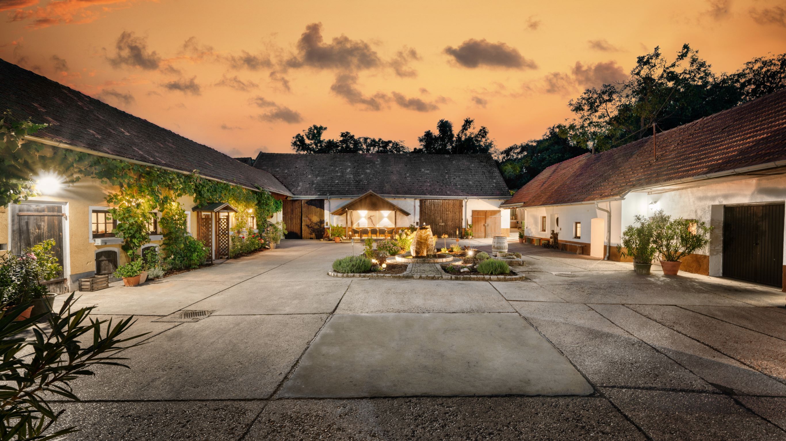 A picturesque courtyard at sunset with illuminated buildings and a central fountain.