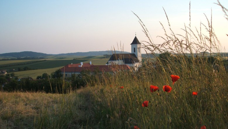 Landschaft mit Kirche und Mohnblumen im Vordergrund.