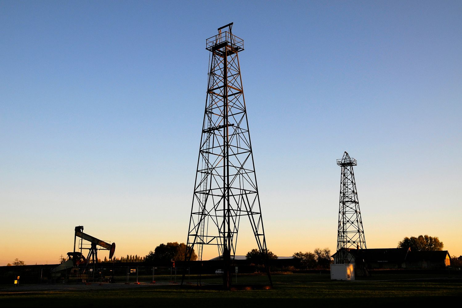 Zwei Bohrtürme und eine Ölpumpe bei Sonnenuntergang.