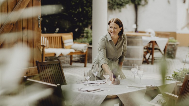 Woman sets table outdoors with wine glasses and napkins.
