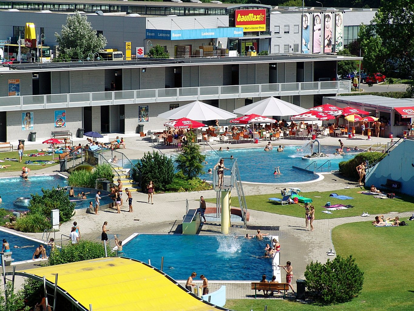 Außenbereich eines Schwimmbads mit mehreren Pools und Liegewiese.