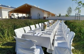 Langer, gedeckter Tisch im Freien vor einem modernen Gebäude mit Holzveranda.