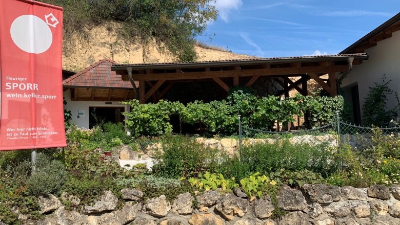 Exterior view of a wine tavern with garden and advertising sign.