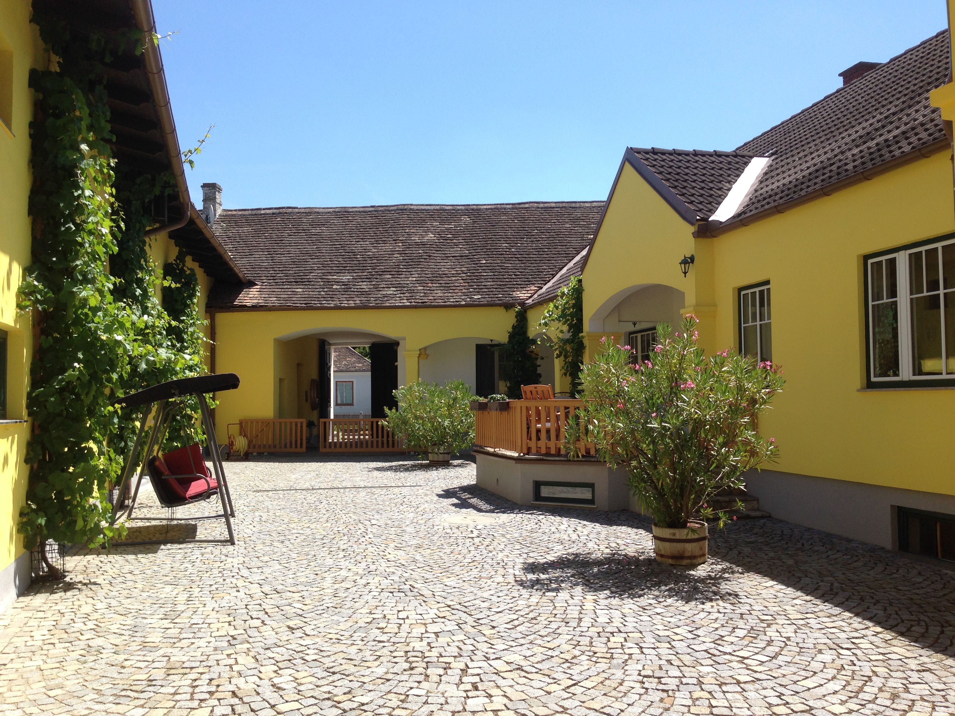 Innenhof eines gelben Winzerhofs mit Pflastersteinen, Schaukel und Pflanzen.